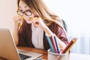 Woman chewing on pencil infront of laptop